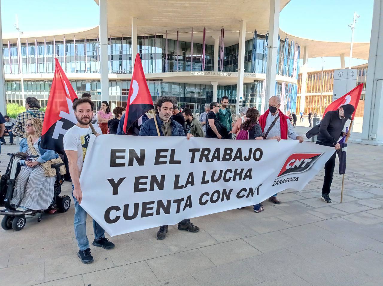 Concentración de personas con banderas de CNT y un cartel en el que se lee "En el trabajo y en la lucha cuenta con CNT", con motivo del juicio de dos militantes que retiraron placas fascistas de las calles de Zaragoza