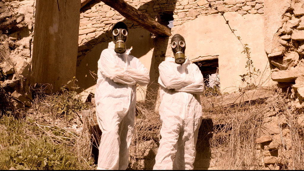 Dos personas que pertenecen al grupo de rap hijos del lindano posan con actitud desafiante con trajes y mascaras de gas en el exterior de las instalaciones de inquinosa en samianigo