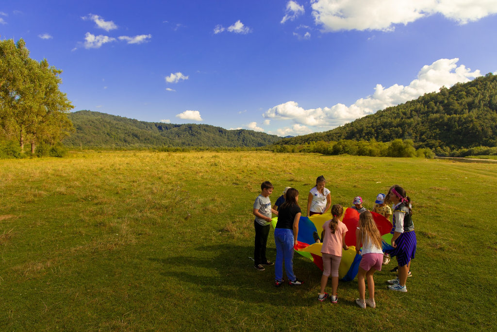 Un grupo de niños y monitoras juegan en un campamento al aire libre rodeados de naturaleza