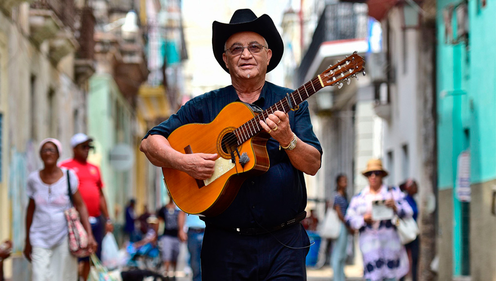 El musica de jazz eliades ochoa andando por la calle con una guitarra
