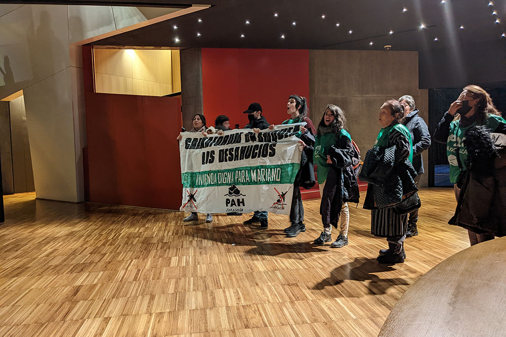 varias personas dentro de caixa forum con una pancarta