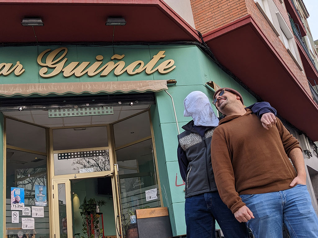 dos integrantes de guiñote de qontaqto se miran a los ojos, uno lleva una malla en la cara, frente al bar guiñote