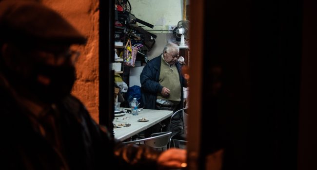 Pepe sale del local de un vecino, donde se han sentado tras ser desahuciados,  para ir a hacer el registro de esa noche en el hostal, gestionado y pagado gracias al apoyo ciudadano. Mientras tanto, Benito, con dificultades de movilidad, se queda esperando solo. Foto: © Cris Aznar