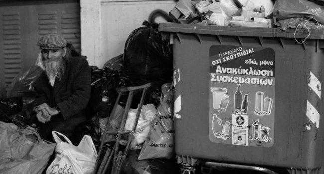 Un hombre junto a un cubo de basura en Grecia. Foto: ANDREAS KONTOKANIS