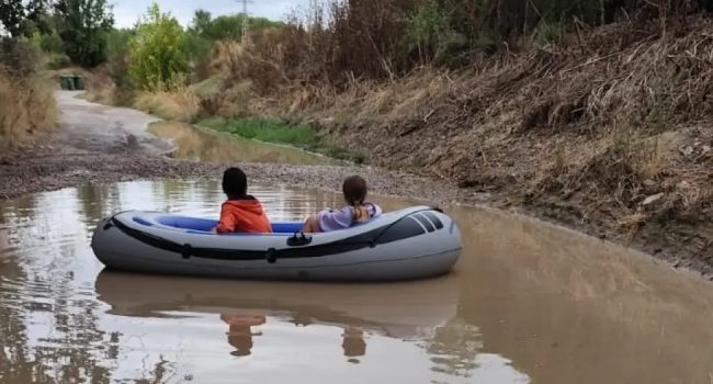 A casa en barca. Dos jóvenes flotan en una barca hinchable dentro de un bache inundado del camino como acto de protesta | Foto: Cambiar Huesca