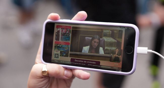 Una manifestante sigue desde su teléfono la intervención de Míriam Nogueras, portavoz de Junts en el Congreso, durante el debate de los decretos de vivienda | Foto: Sindicato de Inquilinas de Madrid