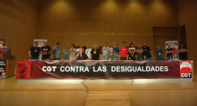 Varias personas de CGT sentadas en una mesa larga, otras detras, una en un atril, en el escenario del world trade center de zaragoza