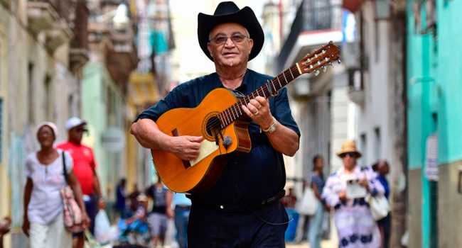El musica de jazz eliades ochoa andando por la calle con una guitarra