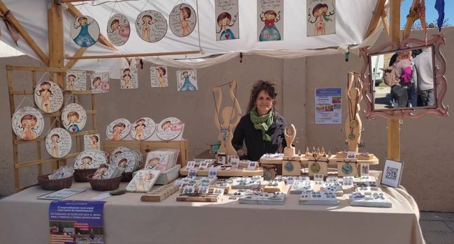 Una mujer emprendedora rural en un puesto de un mercadillo con platos y demas menaje sobre la mesa, parte de una actividad de fademur