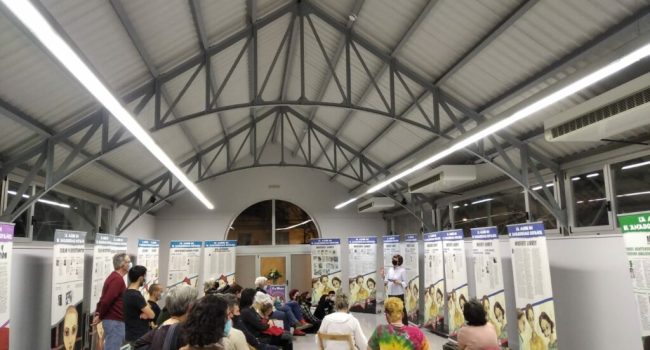 La exposición sobre la mujer en el anarquismo en la sede de CGT con varios paneles y varias personas sentadas durante la presentación