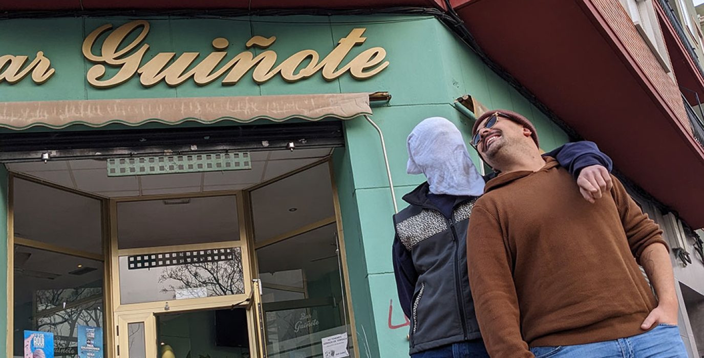 dos integrantes de guiñote de qontaqto se miran a los ojos, uno lleva una malla en la cara, frente al bar guiñote