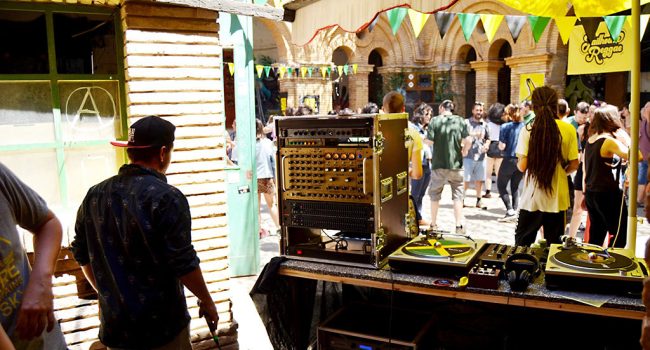 un dj de jailhouse reggae con una mesa de sonido y gente bailando de fondo