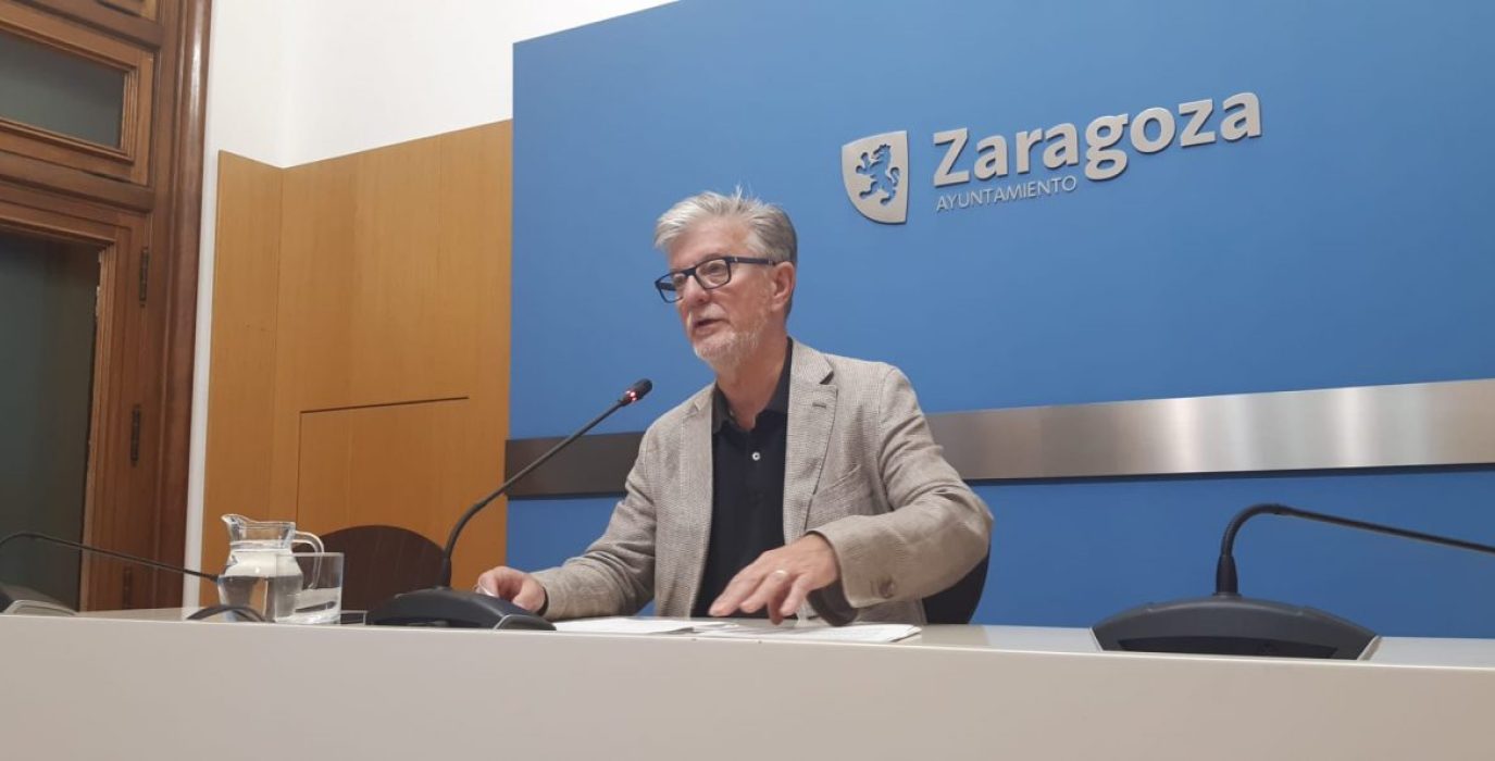 Pedro Santisteve sentado en rueda de prensa con el logo del ayuntamiento de zaragoza detrás