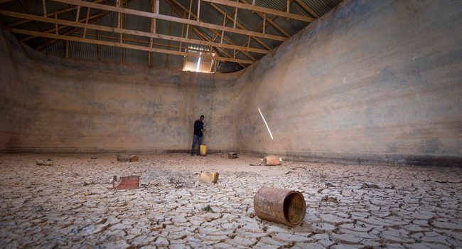 Ahmed, miembro del personal de Oxfam, en el almacenamiento de agua en Puntland, proporcionado y construido por Kaalo y Oxfam, se ha secado por completo debido a que la recolección de agua terminó después de la falta de lluvia durante casi cuatro años