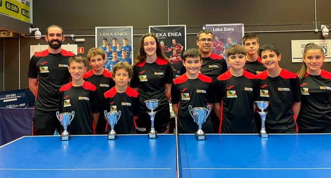 Varios niños y niñas y sus entrenadores posan delante de una mesa de tenis de mesa en representación de la selección de aragón, en la copa pirineos