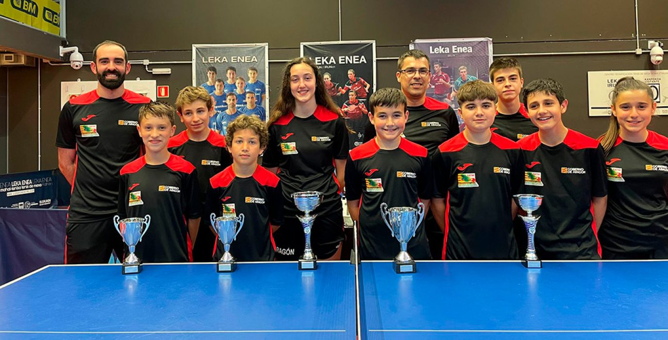 Varios niños y niñas y sus entrenadores posan delante de una mesa de tenis de mesa en representación de la selección de aragón, en la copa pirineos