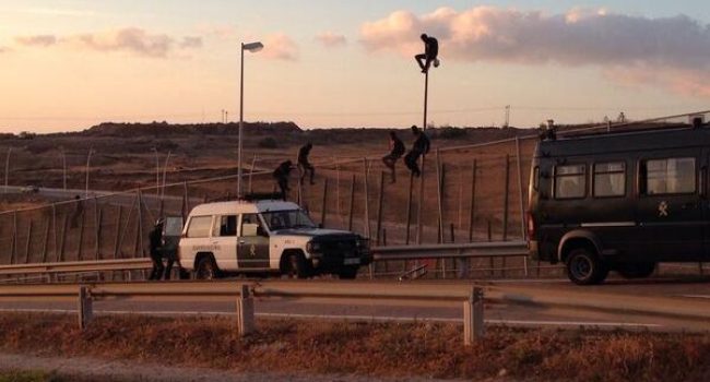 Un migrante, encaramado en una farola situada en territorio español tras saltar la valla de Melilla. Posteriormente fue devuelto. Foto: Popular TV Melilla