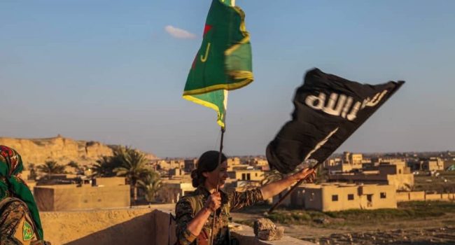 Miliciana kurda reemplaza la bandera del Daesh con una de las Unidades Femeninas de Protección (YPJ) en Baghuz. Foto: ANF