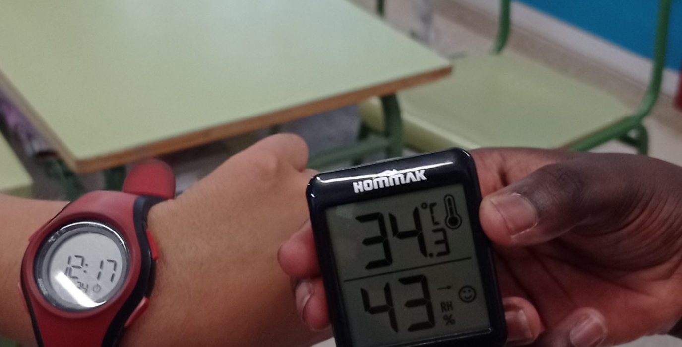 dos manos cogiendo un termómetro en un aula para mostrar que llegaron a temperaturas de 34 grados