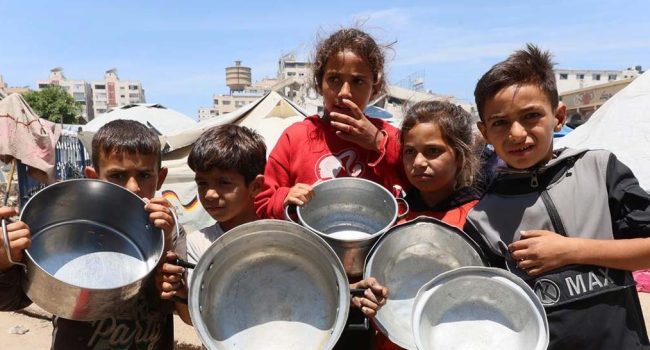 Niños y niñas en Gaza esperando a que les llenen los contenedores vacíos de comida. | Foto: Noticias ONU