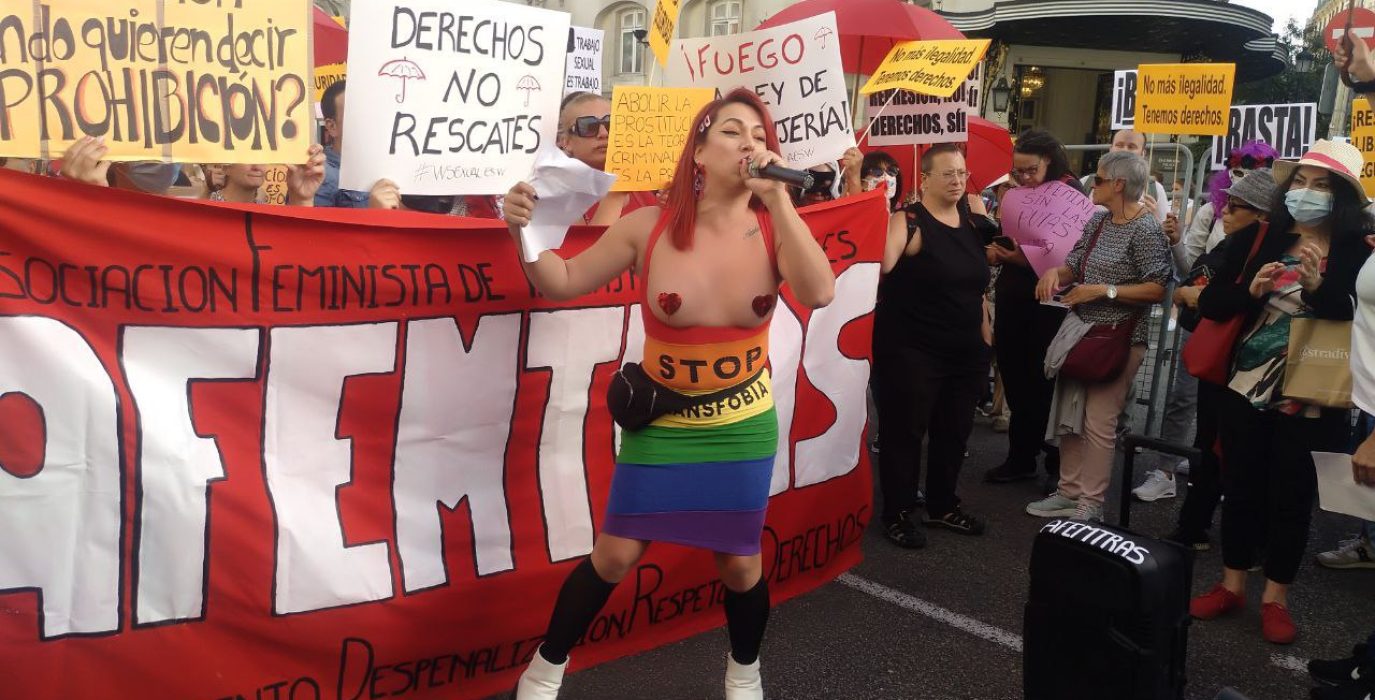 varias personas con carteles en contra de ley rodeando a una trabajadora sexual con un micrófono
