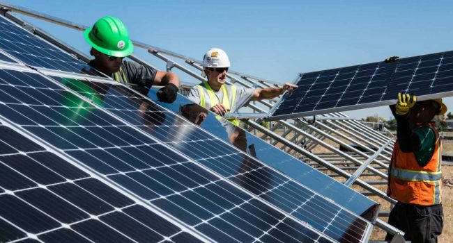 Tres trabajadores instalan una serie de placas solares en un cambpo
