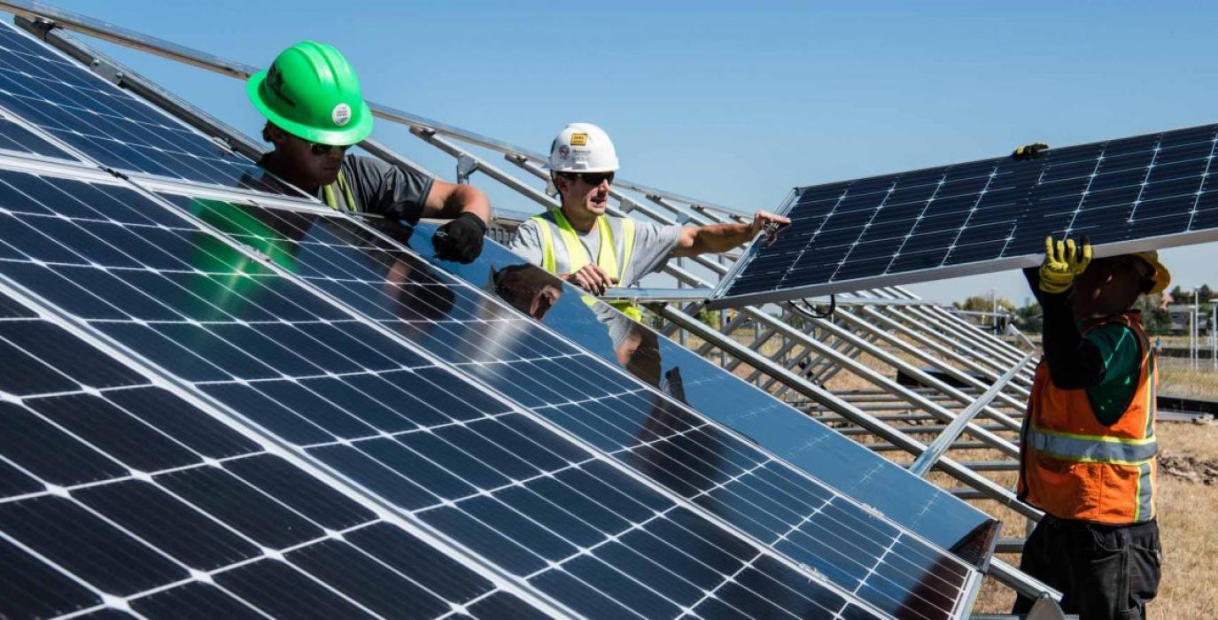 Tres trabajadores instalan una serie de placas solares en un cambpo